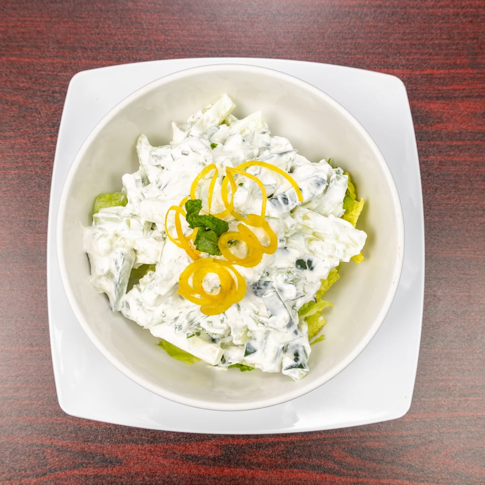 Creamy cucumber salad garnished with lemon zest and mint, served over lettuce in a white bowl.