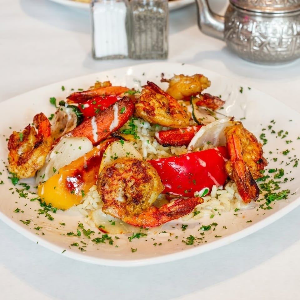 Plate of grilled shrimp, vegetables, and rice garnished with parsley and drizzled with white sauce.
