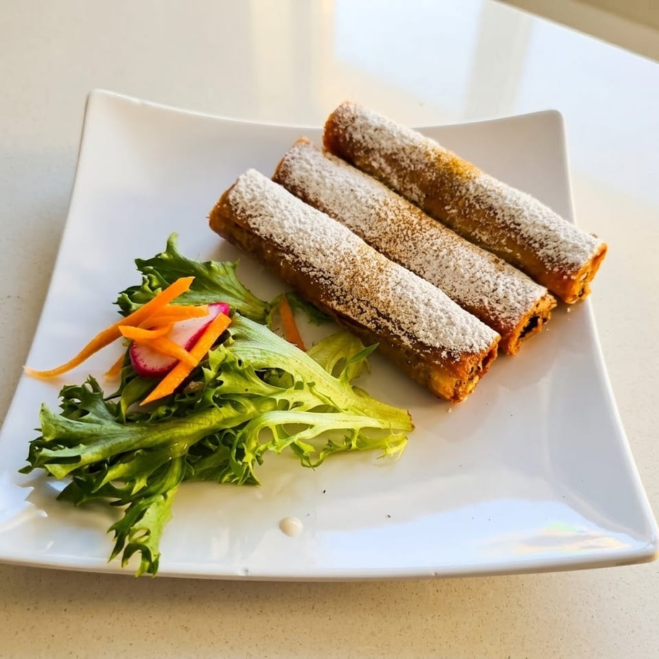 Three powdered-sugar-coated fried rolls served with leafy greens, carrot strips, and sliced radish on a white plate.