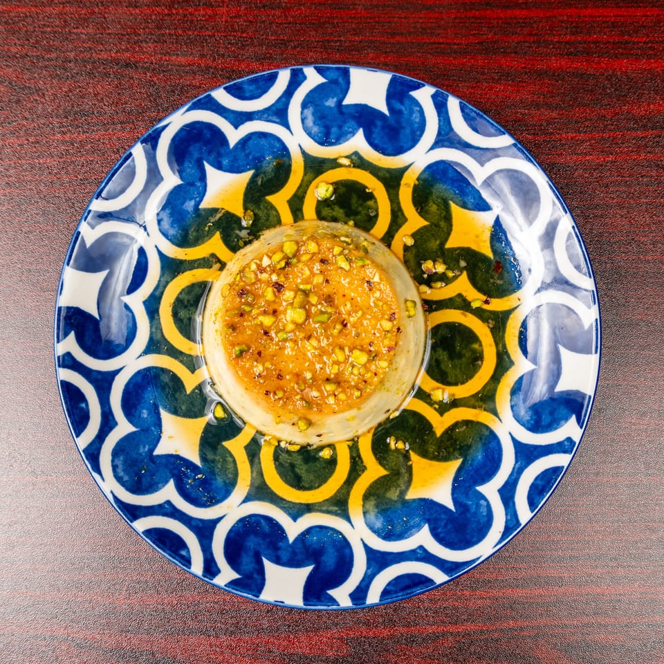 Pistachio-topped dessert in a glass dish, served on a colorful blue, green, and yellow patterned plate.