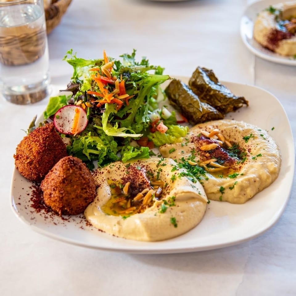 Middle Eastern platter with falafel, hummus, stuffed grape leaves, fresh salad, herbs, spices, and toasted nuts.