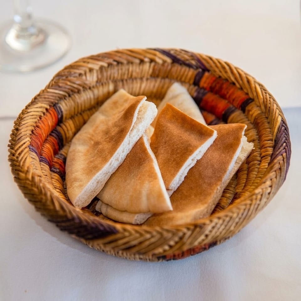 Woven basket filled with triangular pieces of golden-brown pita bread on a white table.